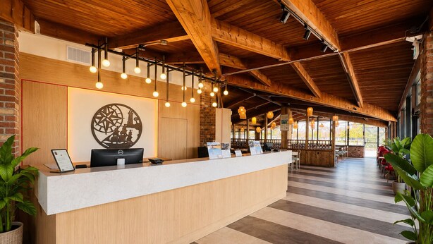 A reception desk with a modern design, a large decorative wall piece, and a spacious area with seating and natural light. - Ramada by Wyndham 1000 Islands/Gananoque (Gananoque)