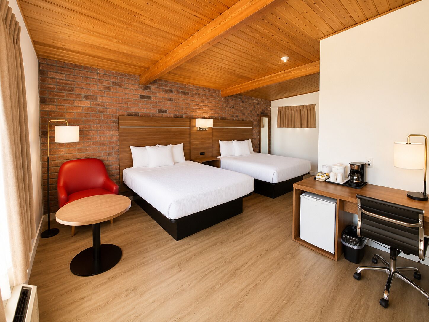 Habitación de hotel con dos camas, una silla roja, un escritorio pequeño con cafetera y un refrigerador compacto.