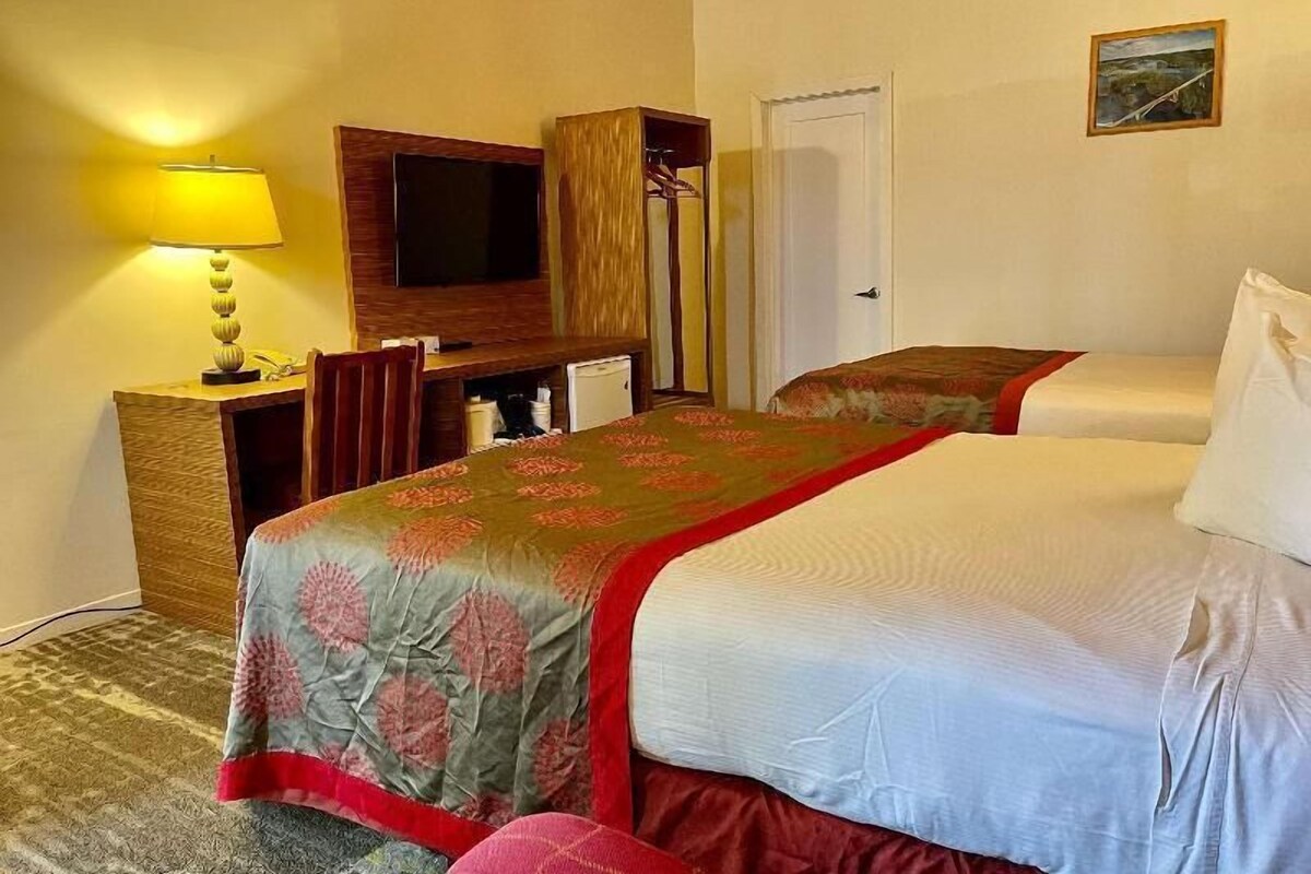 A hotel room with a bed, a desk with a lamp, a television, and a door.