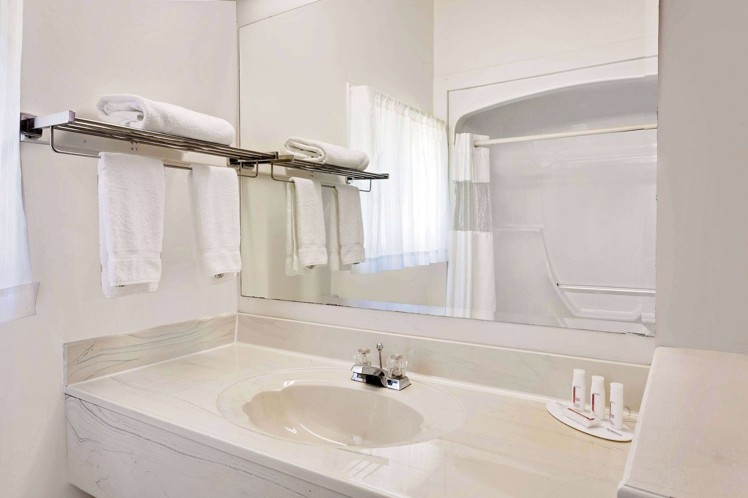 Een badkamer met een marmeren wastafel, een handdoekrek met opgevouwen handdoeken, een spiegel en een douche.