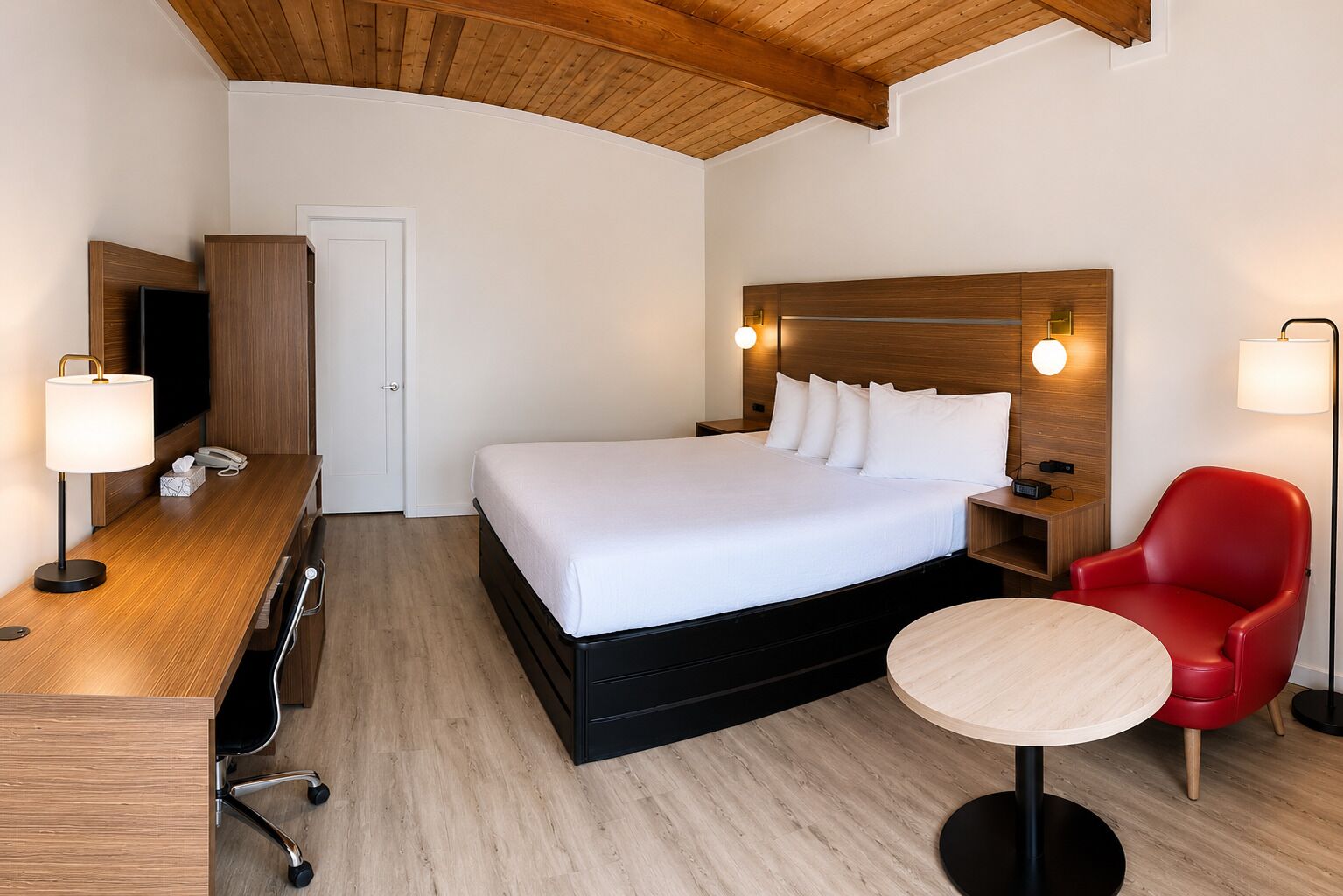 A hotel room with a bed, bedside tables, a desk, a chair, and a TV.