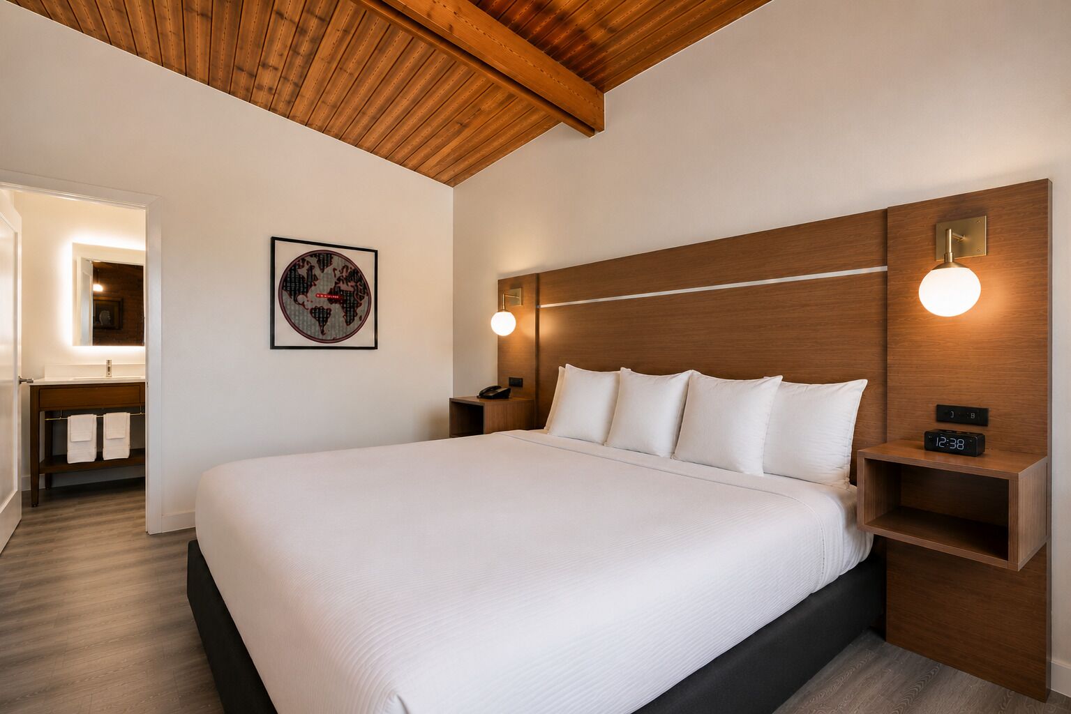A hotel room with a large bed, wooden headboard, bedside tables with lamps, a framed world map on the wall, and a wooden ceiling.