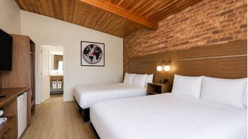 A hotel room with two beds, a wooden ceiling, a brick wall, and a framed picture on the wall.