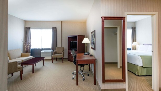 A hotel room with a sofa, a desk, a chair, a TV, a lamp, and a bed. - Ramada by Wyndham St. John's (St. John's)