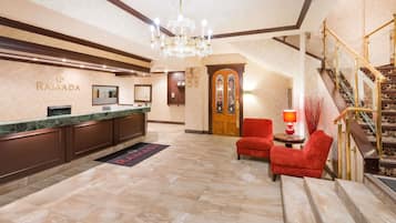 A reception area with a marble floor, a chandelier, a reception desk, a red armchair, and a staircase with a golden railing.