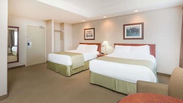 A hotel room with two beds, a round table, a chair, a mirror, and two framed pictures on the wall.