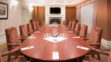 A conference room with a long table, patterned chairs, a flat-screen TV, and a fireplace.