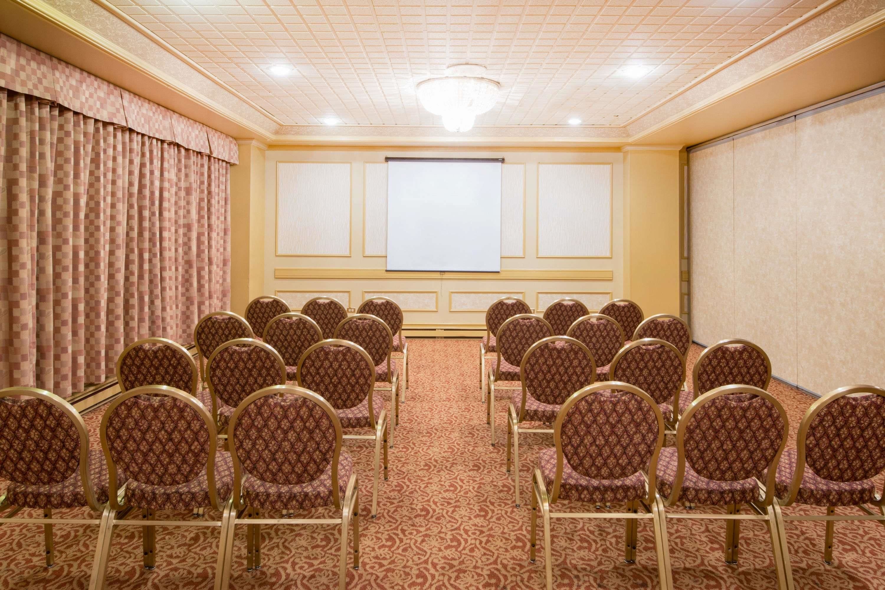 Un salón de conferencias con filas de sillas, una pantalla de proyector y piso alfombrado.