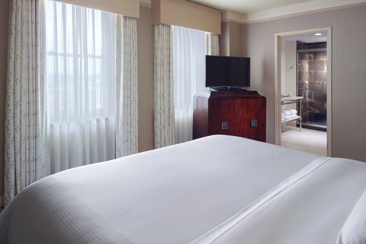 A hotel room with a large bed, a television on a wooden cabinet, and a bathroom visible through an open door.