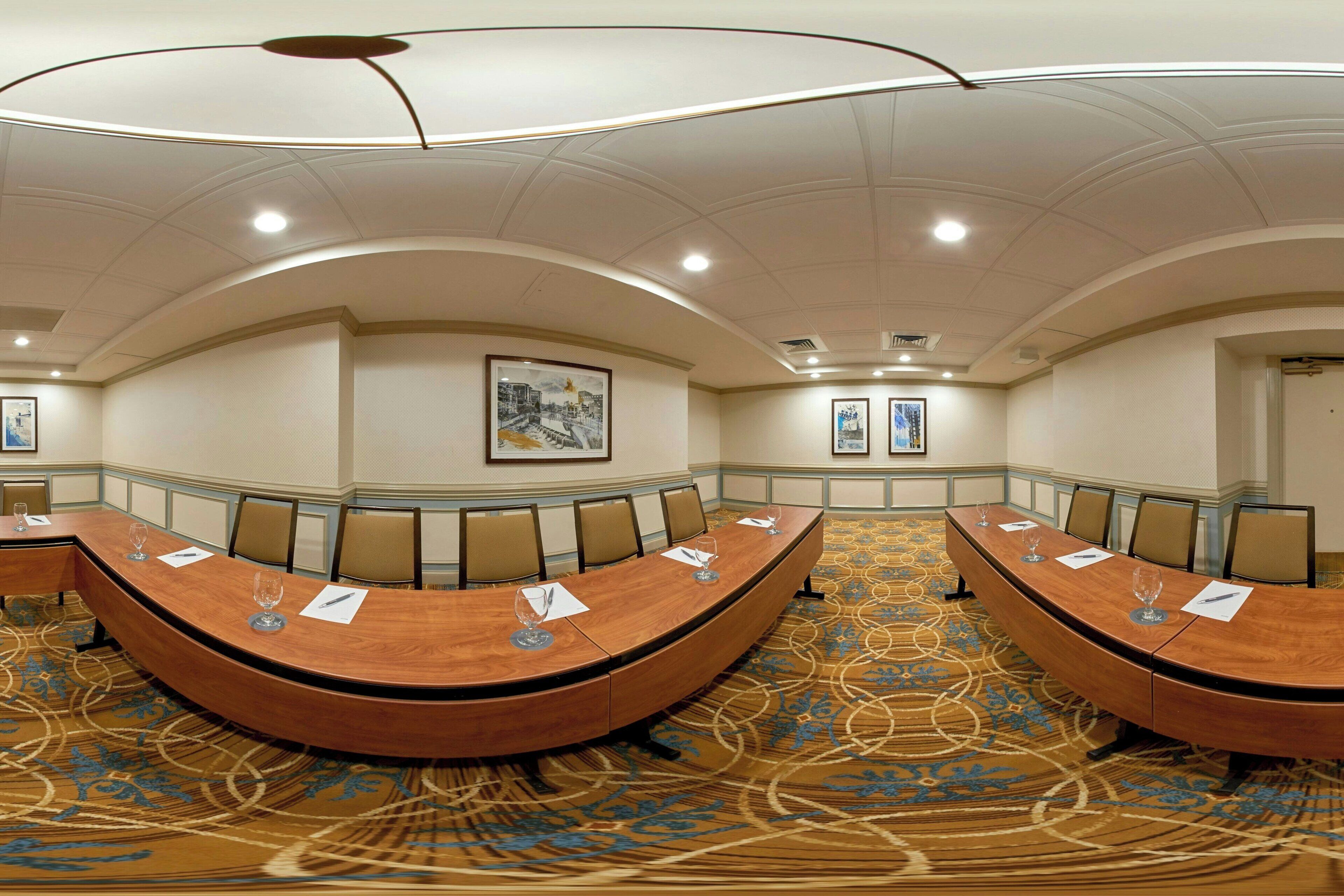 A conference room with a large oval table, chairs, and framed artwork on the walls.