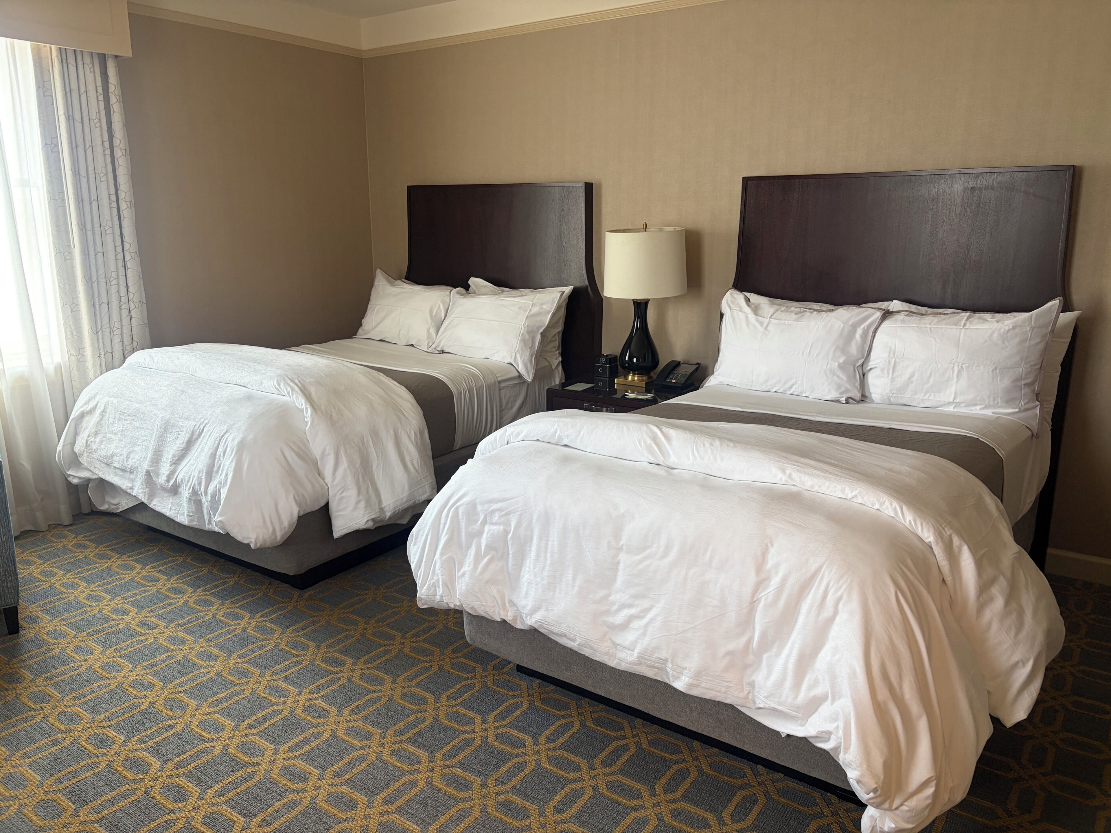A hotel room with two beds, a nightstand with a lamp, and a patterned carpet.