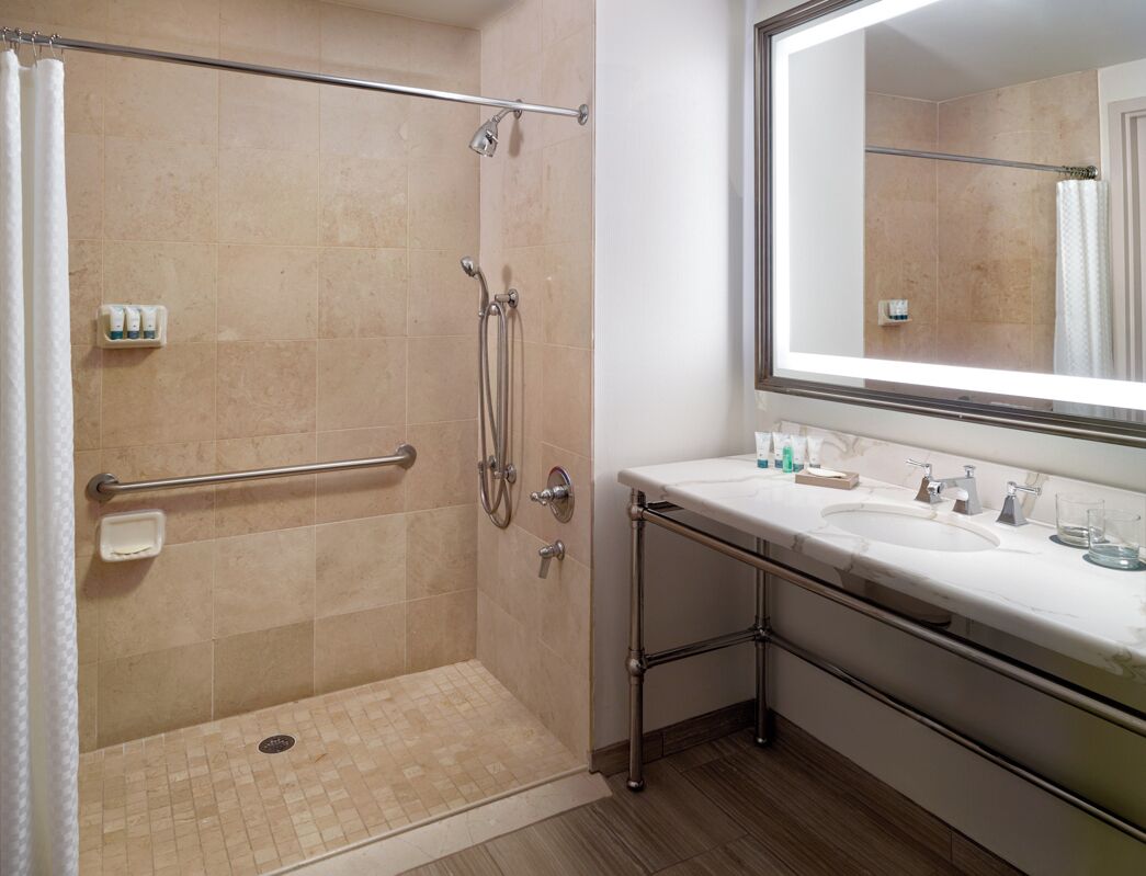 Un baño con cabina de ducha, un espejo grande y tocador con lavabo y artículos de aseo.