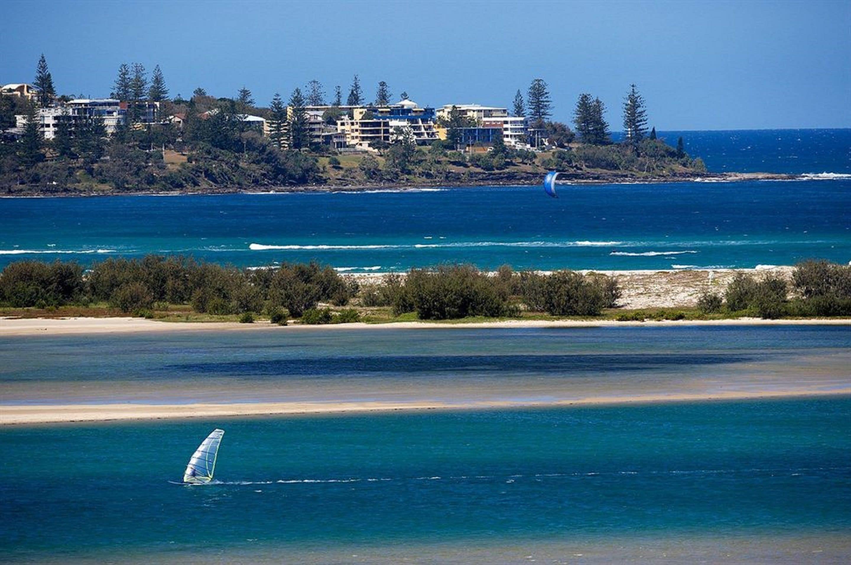 A coastal view with a beach, ocean, and a windsurfing board.