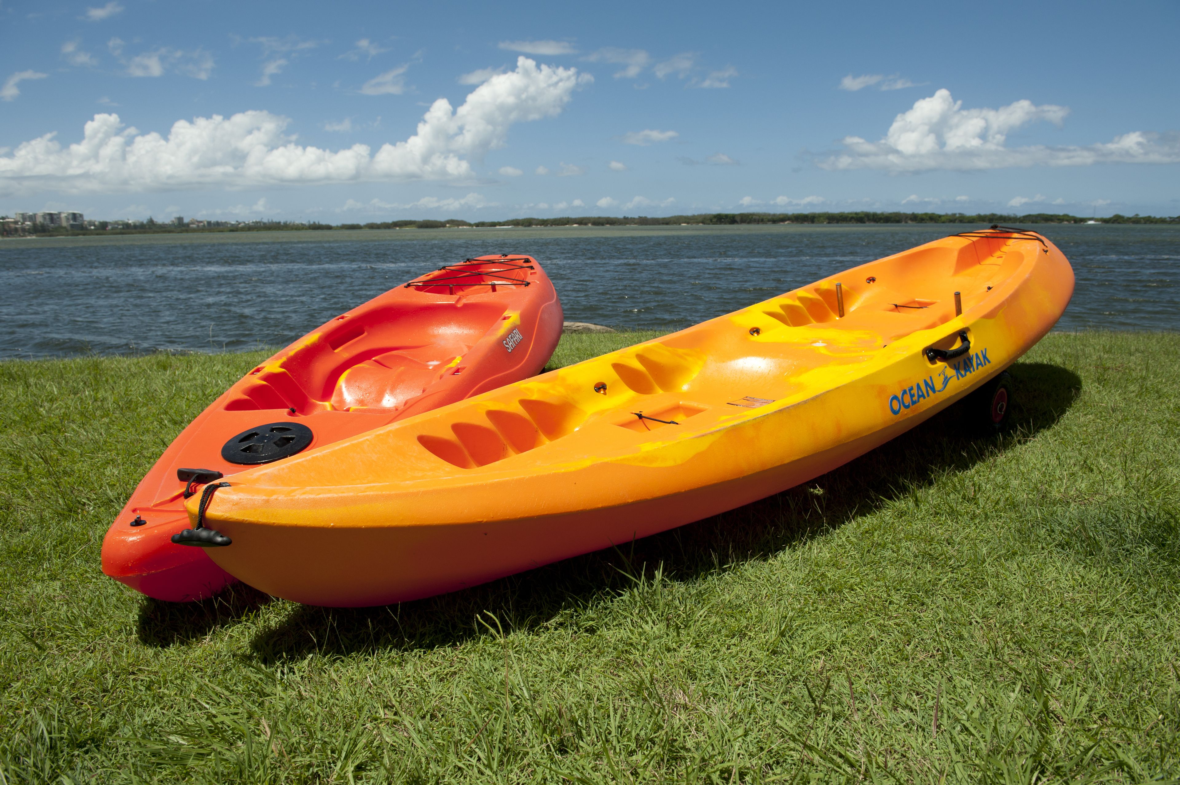 Deux kayaks sont posés sur une zone herbeuse, près d’une étendue d’eau.