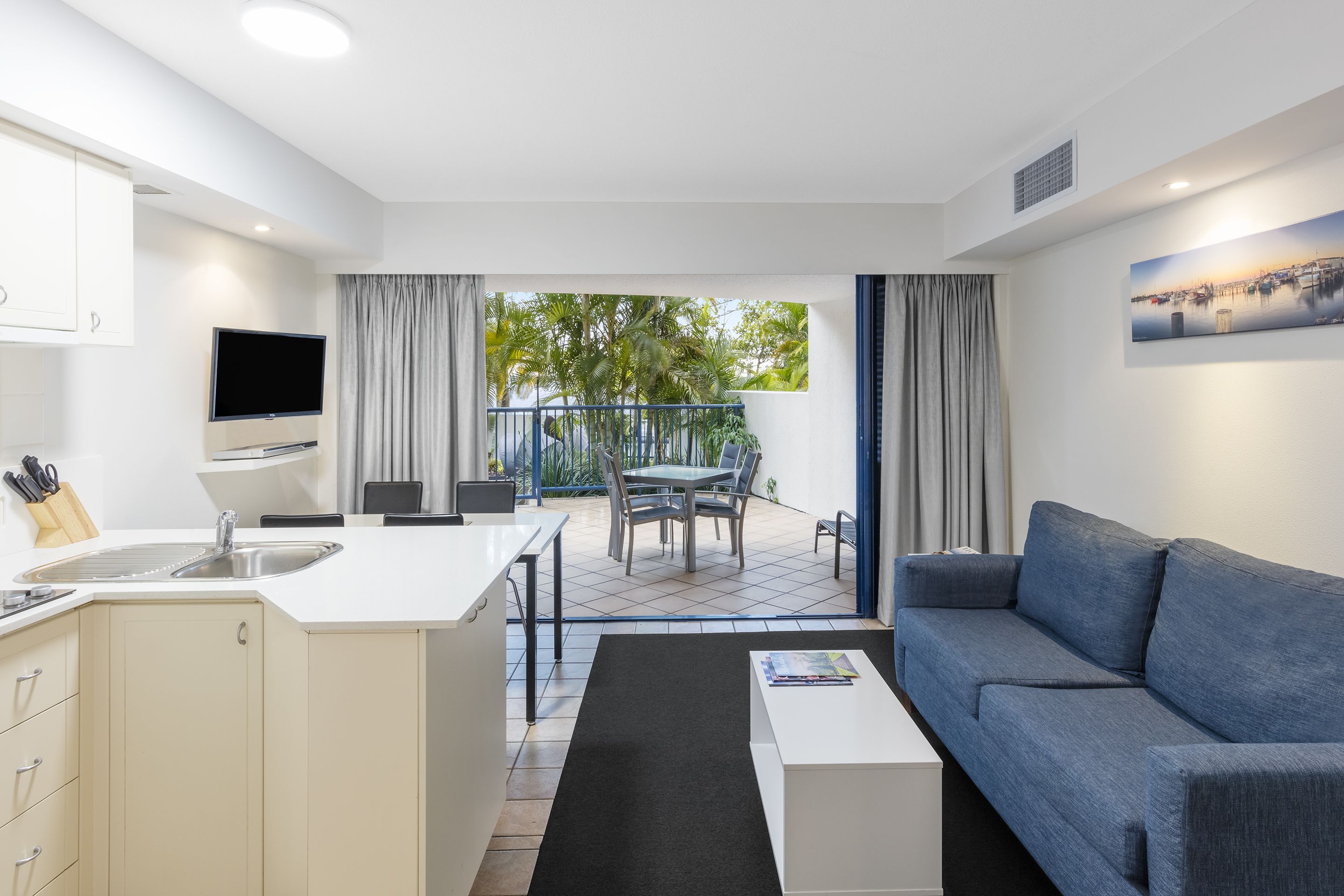 A modern living space with a kitchen, dining area, and a balcony with a view of greenery.