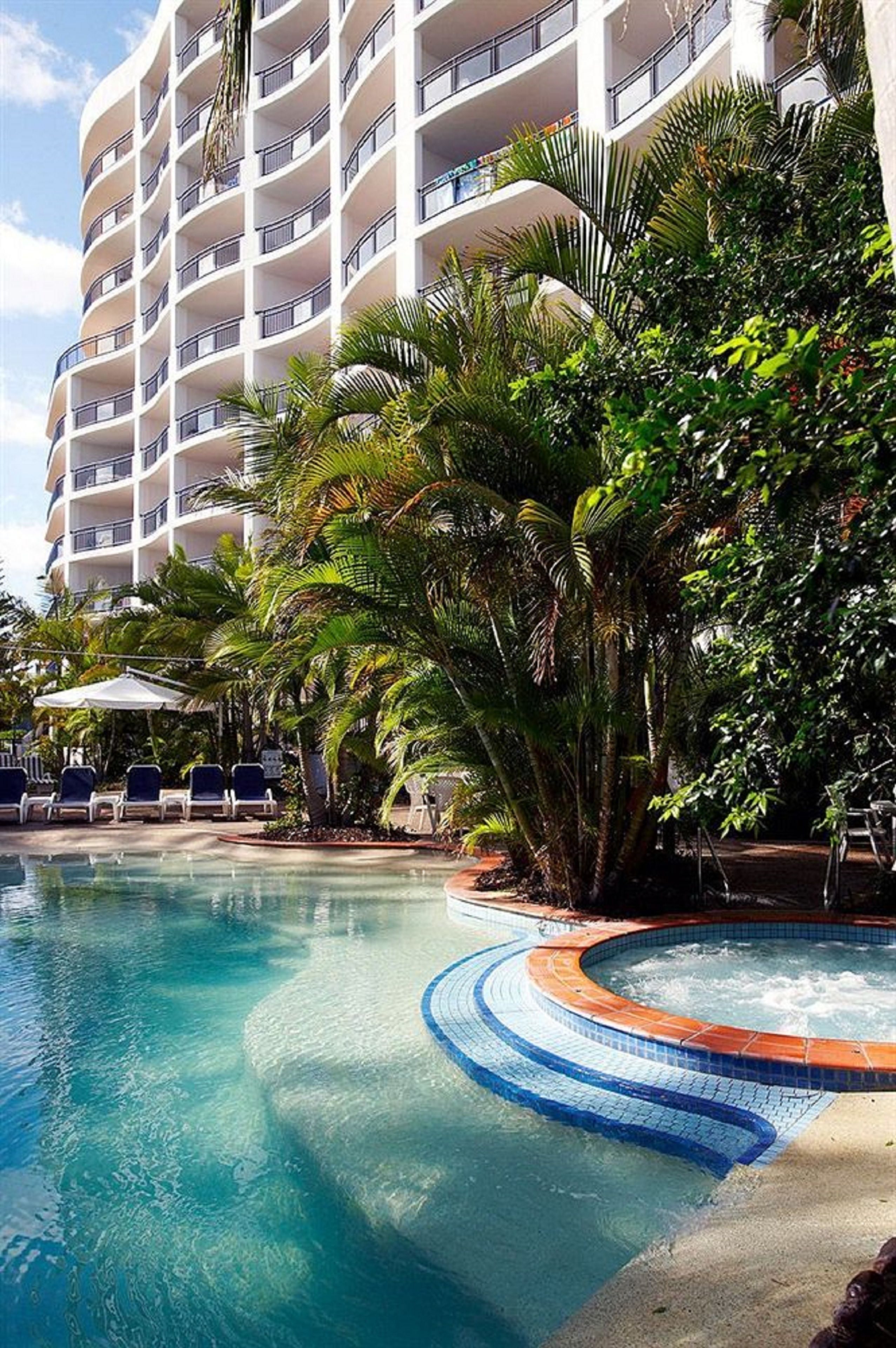 A hotel with a large pool, surrounded by palm trees and lounge chairs.