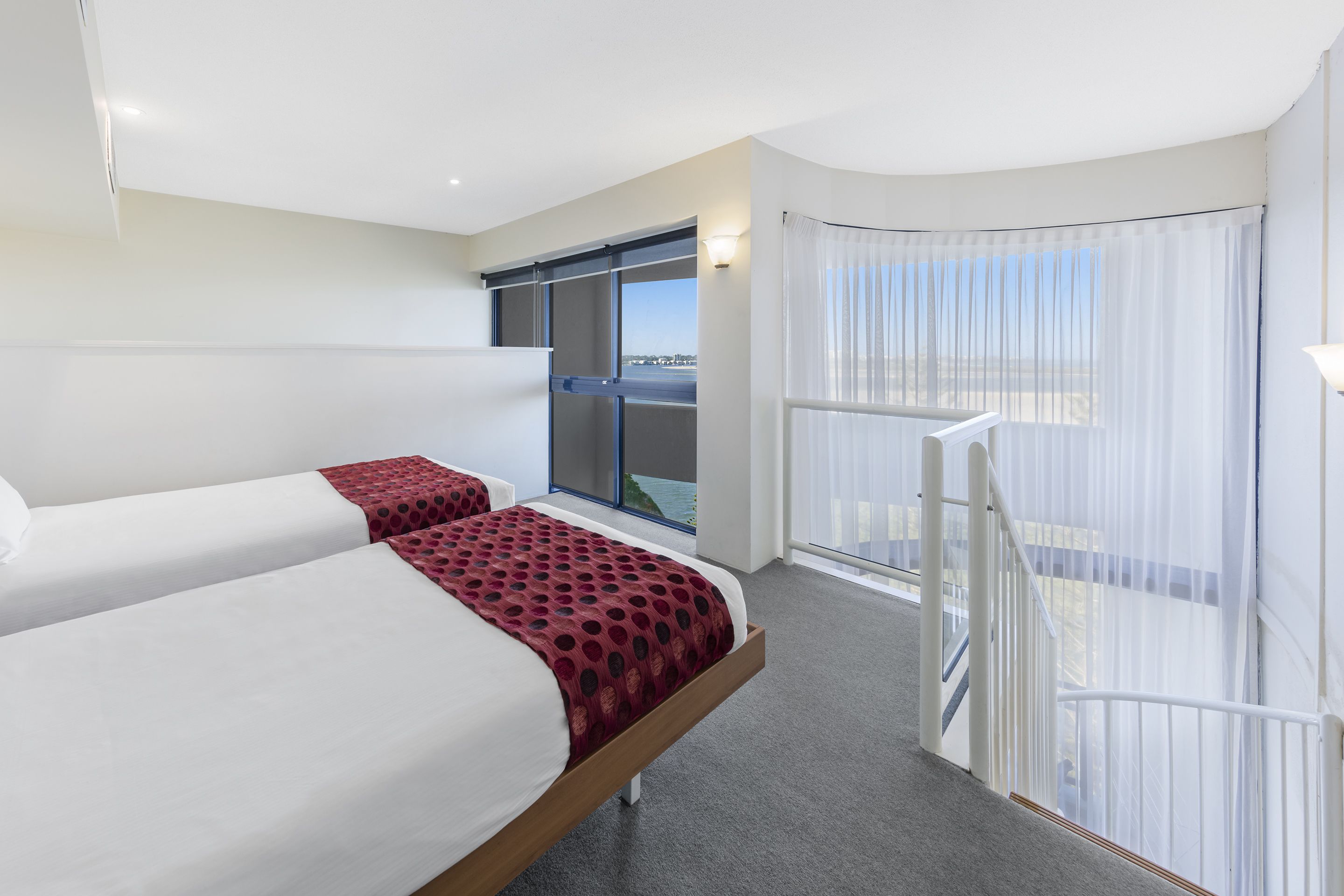 Quarto de hotel com duas camas, varanda com vista e uma janela grande.