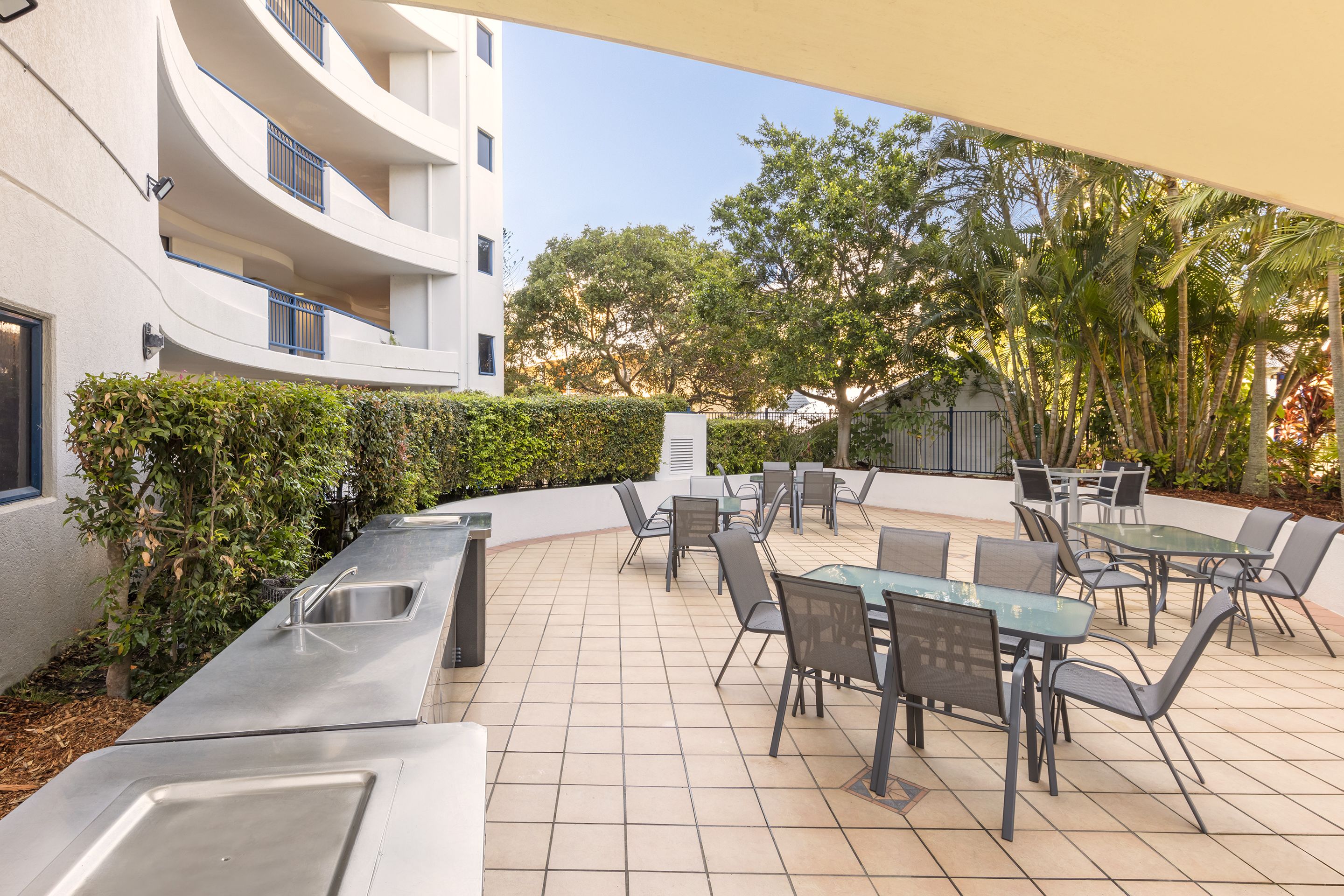 Un patio exterior con zona de comedor, mesas y sillas, y una cocina integrada con lavamanos.