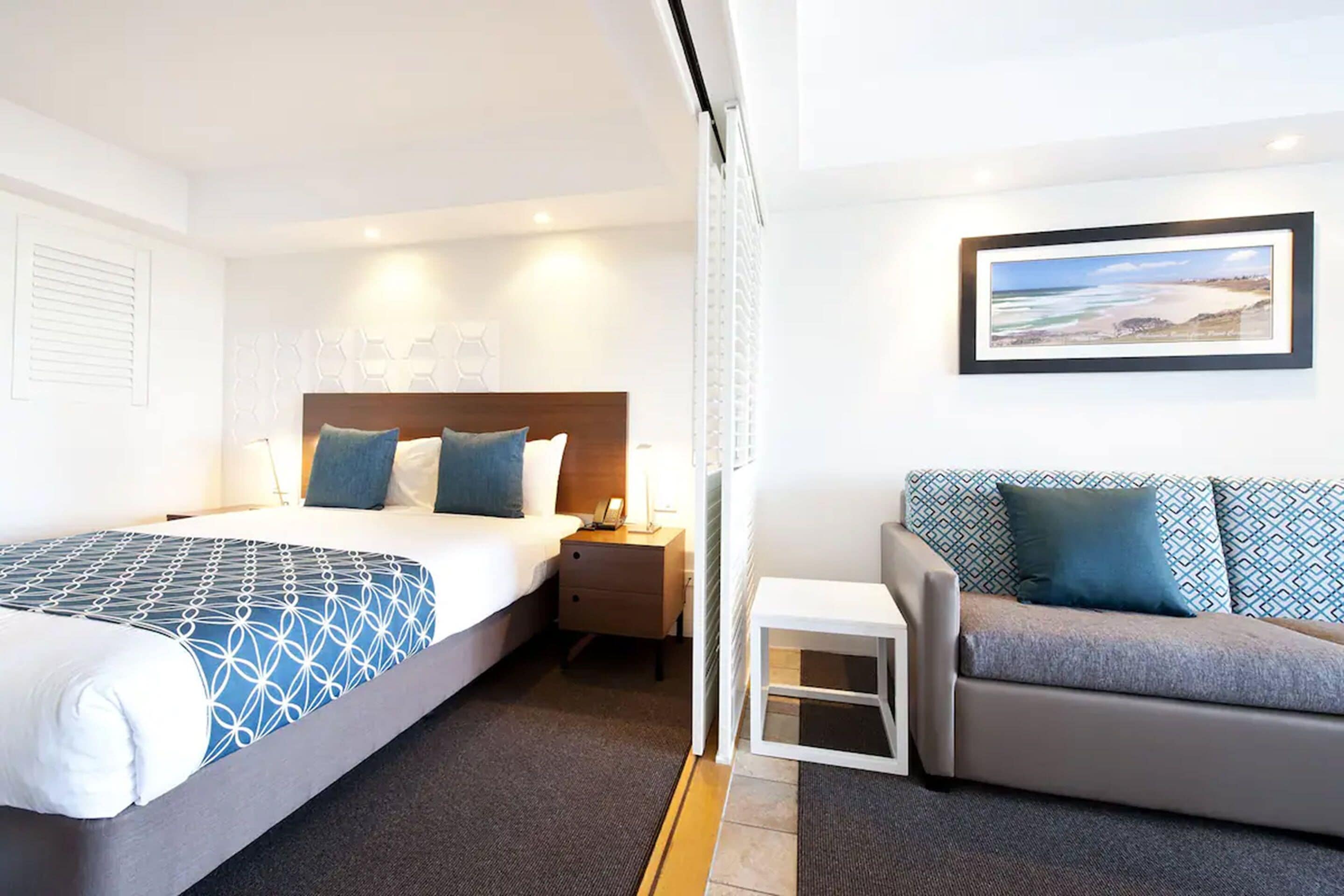 A hotel room with a bed, a nightstand, a sofa, and a small table.