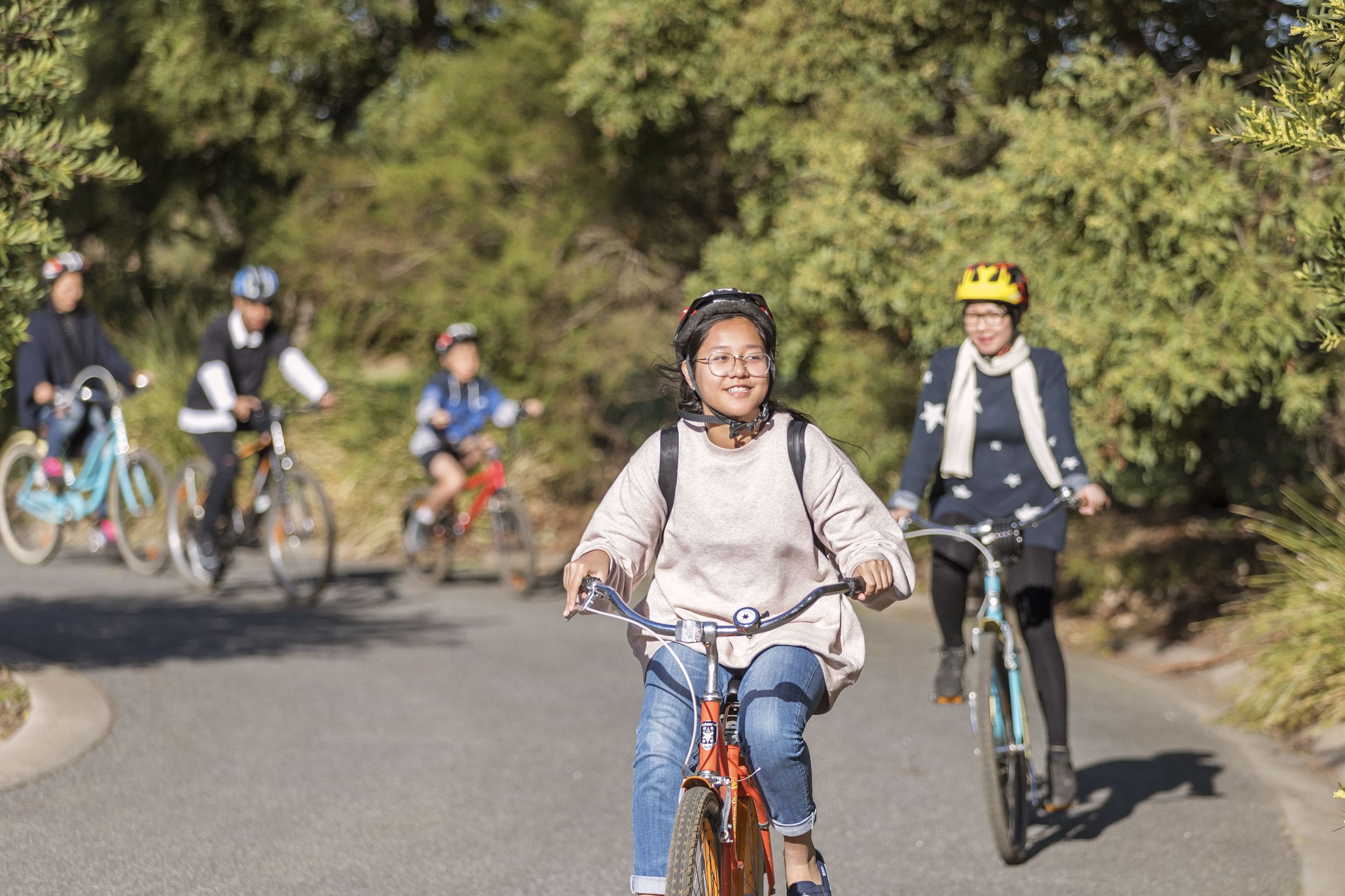 Un grupo de ciclistas en un sendero pavimentado rodeado de árboles.