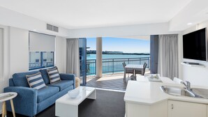 Ein modernes Hotelzimmer mit Balkon und Blick auf ein Gewässer, einem Essbereich und einer Küchenzeile.