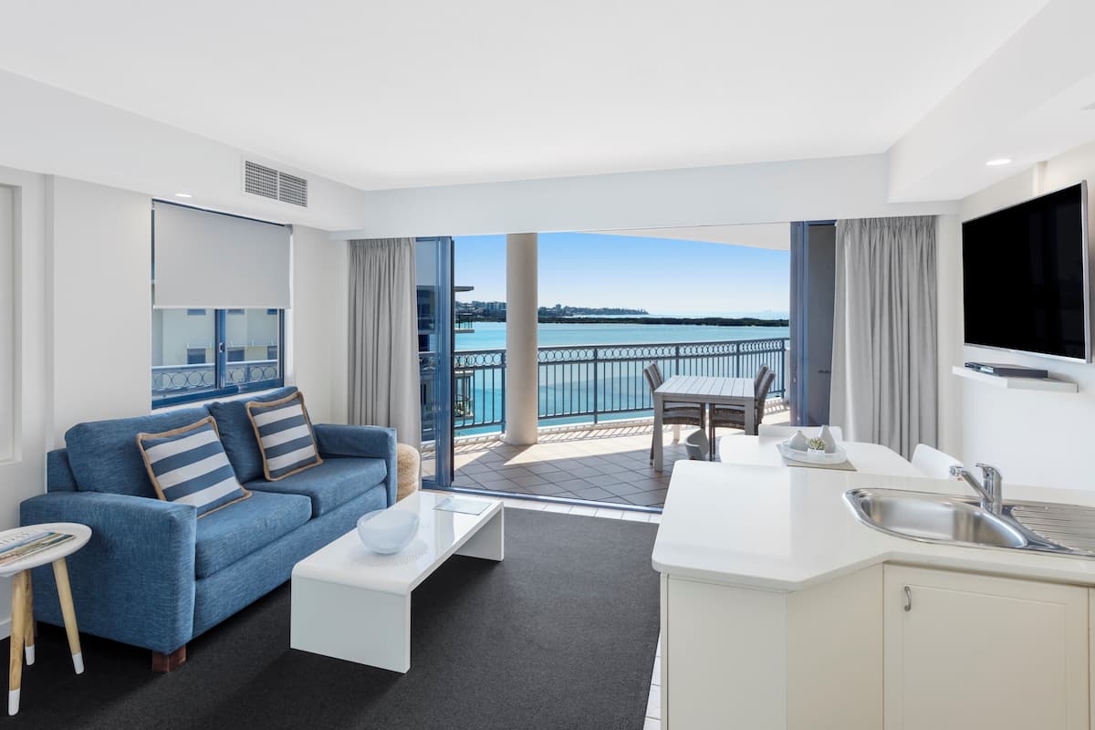 Une chambre d’hôtel moderne avec balcon donnant sur un plan d’eau, un coin repas et une kitchenette.