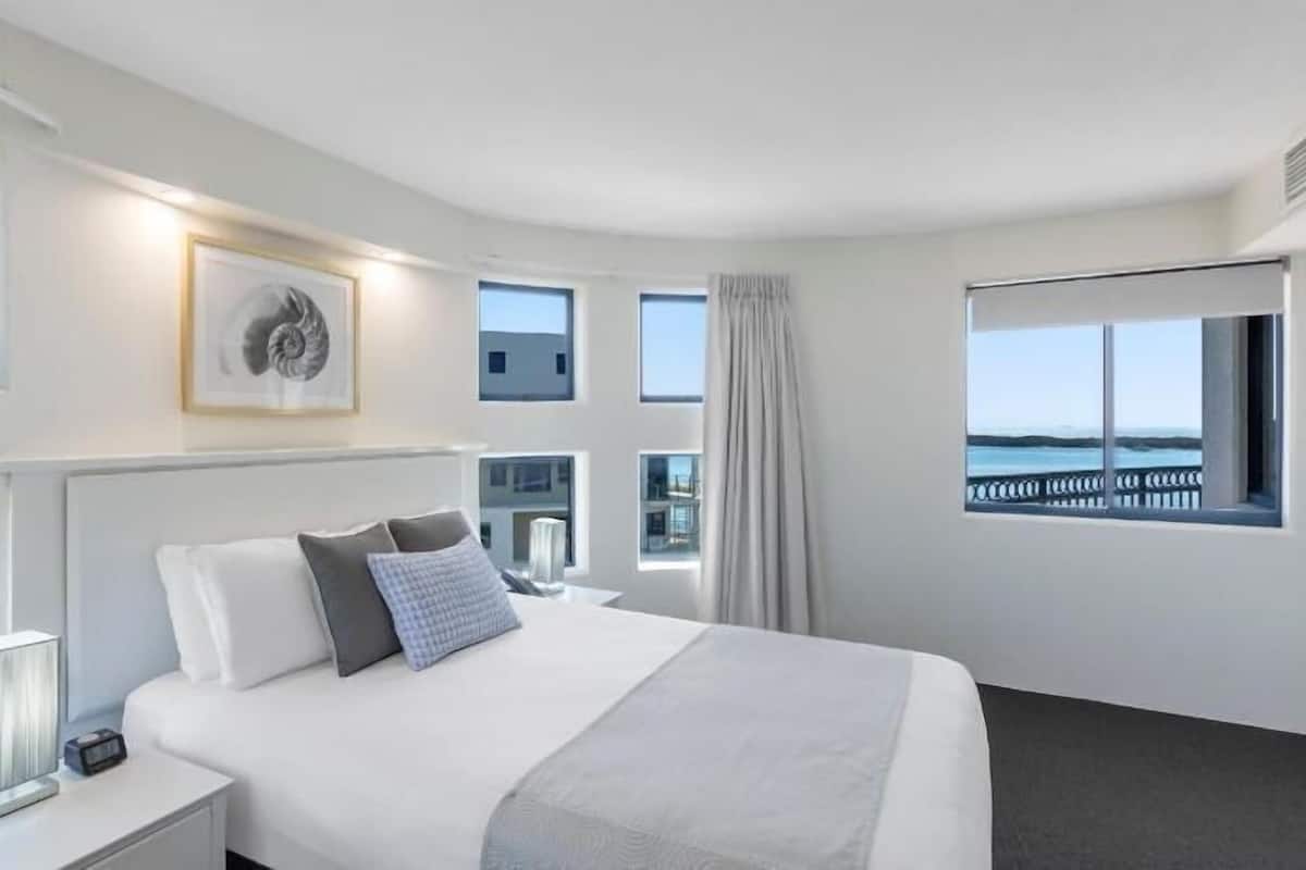 Une chambre d’hôtel moderne avec un grand lit, une table de chevet, un tableau encadré et une vue sur la mer.