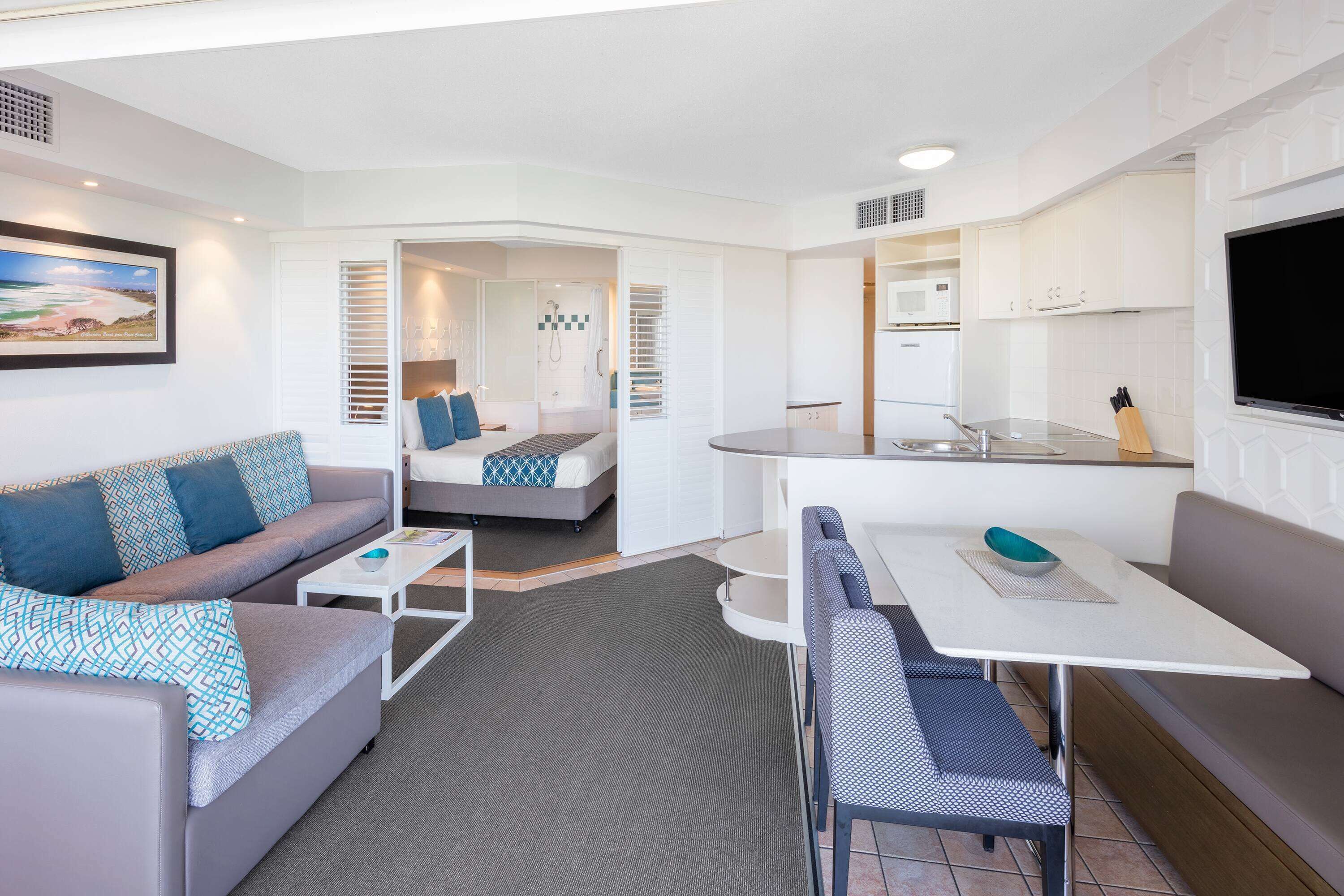 Un espacio habitable compacto con sofá, cama, mesa de comedor y kitchenette.