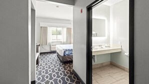 Une chambre d’hôtel avec un lit, une salle de bain dotée d’un lavabo et d’un miroir, et un sol à motifs.