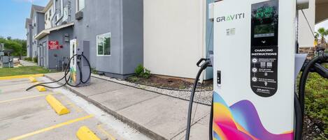 A charging station with instructions, a building with a grey facade, and a parking area with yellow lines.