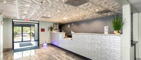 A reception area with a modern design, featuring a patterned ceiling, a reception desk, and a plant.