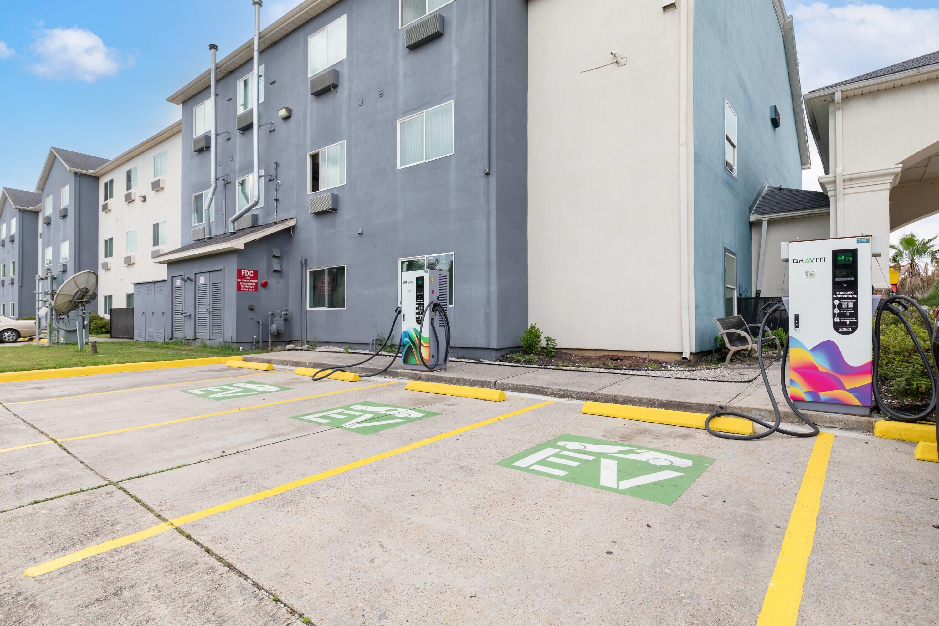 A parking area with electric vehicle charging stations, marked EV parking spaces, and a building with multiple floors and balconies.