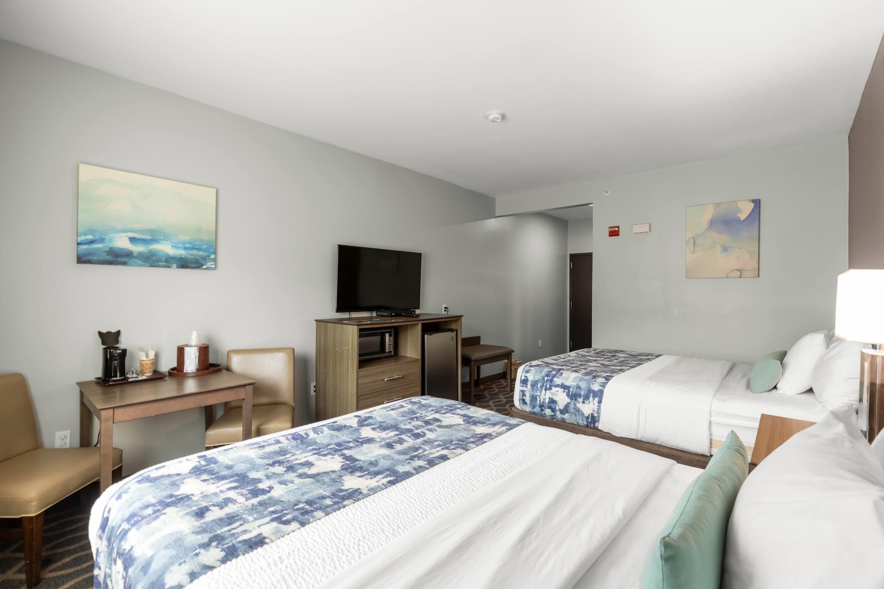 Ein Hotelzimmer mit zwei Betten, einem Schreibtisch mit Fernseher, einer kleinen Sitzecke und Bildern an den Wänden.