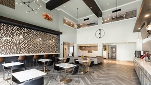 Un hall d’hôtel moderne avec un parquet en bois disposé en chevrons, un comptoir d’accueil et un espace détente comprenant des tables et des chaises.