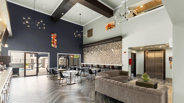 Un hall d’hôtel moderne avec un parquet en bois disposé en chevrons, un canapé d’angle et un coin bar avec des tabourets.