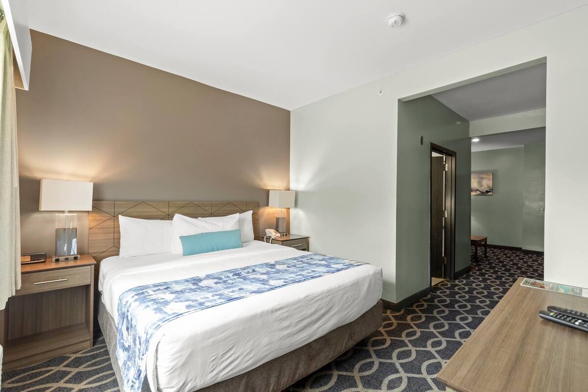Een hotelkamer met een groot bed, nachtkastjes met lampen, een bureau met stoel, en een kamer met een patroon vloer.