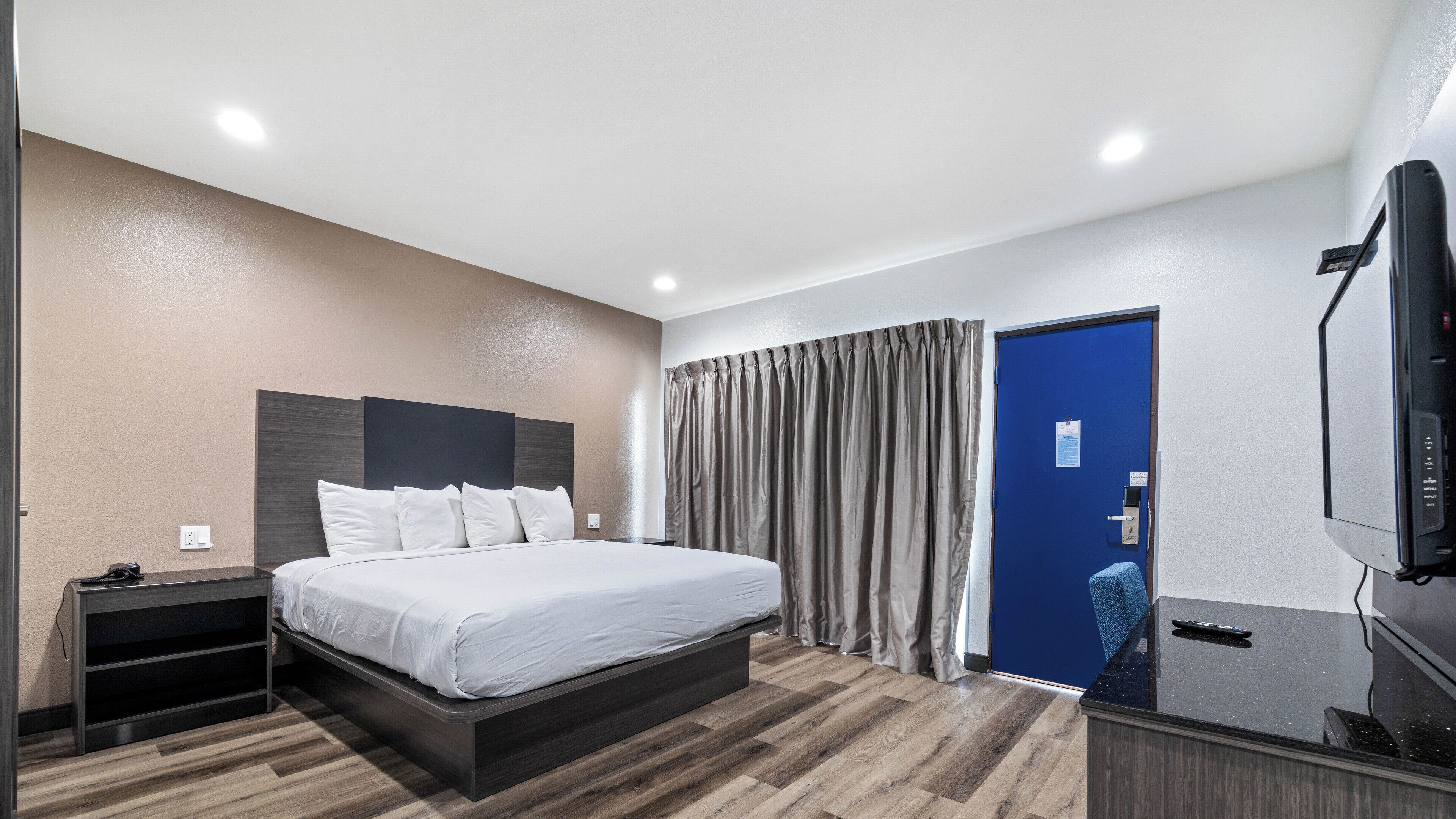 A hotel room with a bed, a desk, a television, and a blue door.