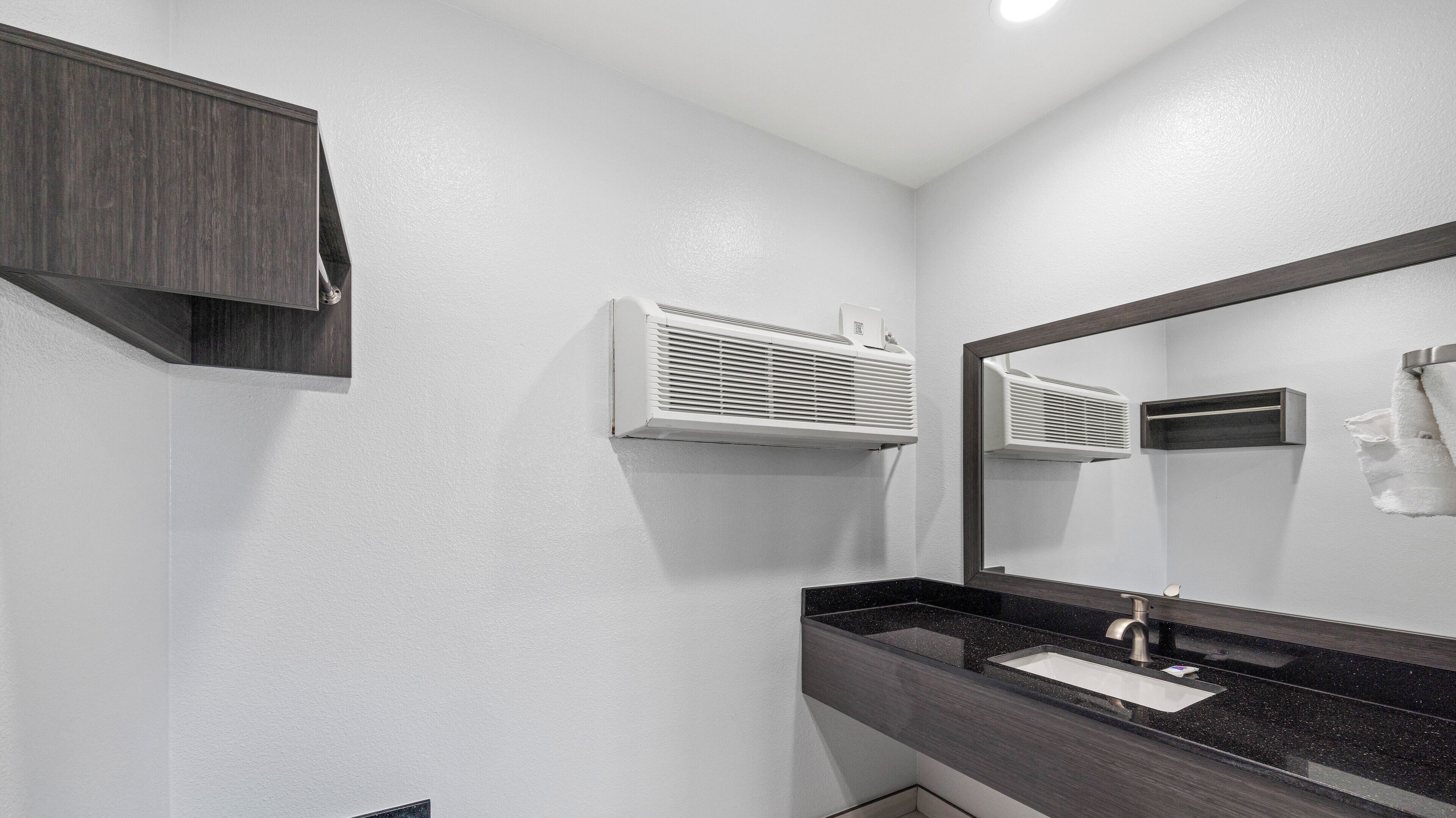 A modern bathroom with a dark wood vanity, a white sink, and a large mirror.