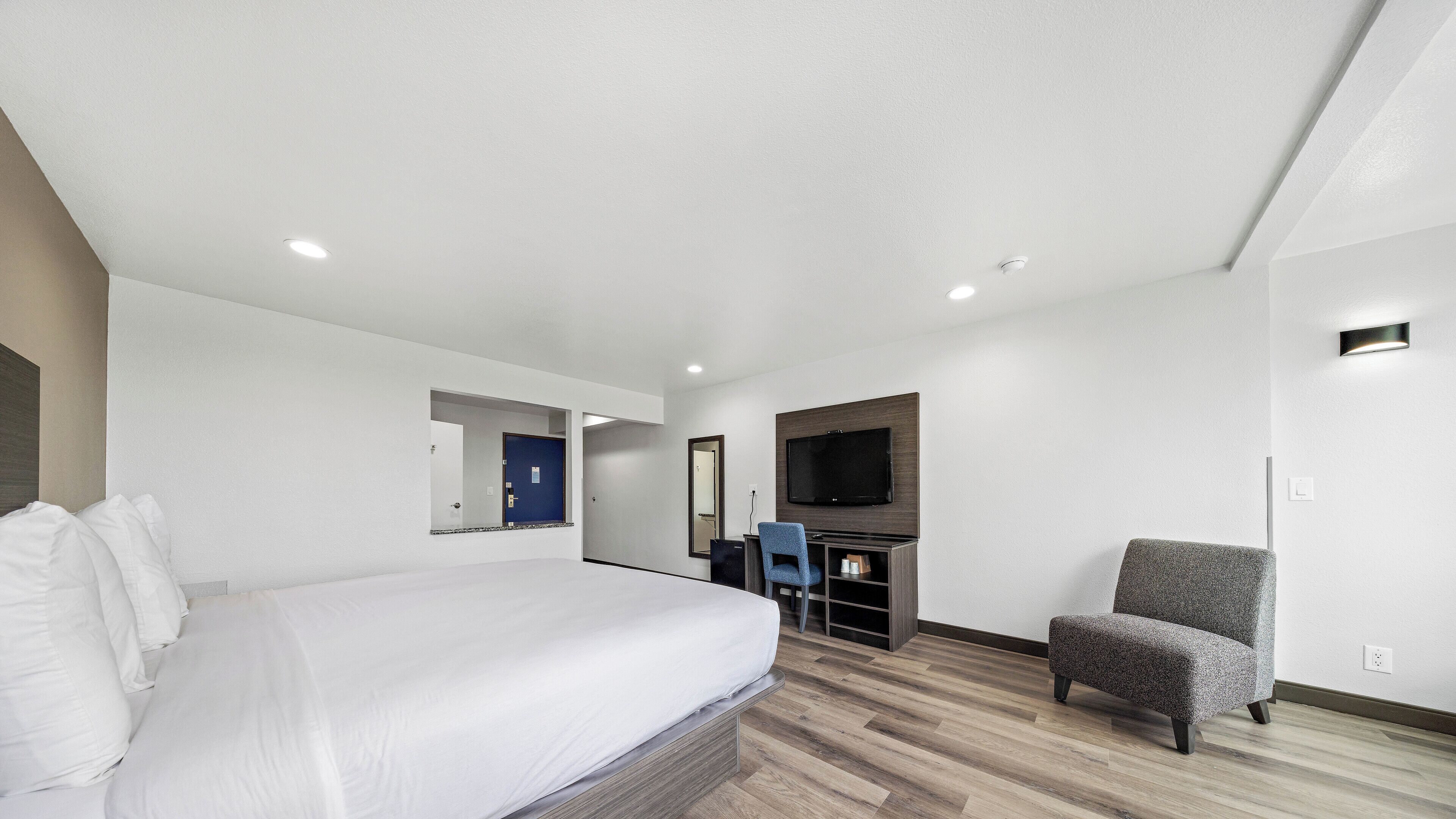 A hotel room with a bed, a TV mounted on the wall, a chair, and a small desk.