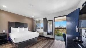 A modern hotel room with a large bed, a desk, a chair, and a balcony with a view of the city. - Motel 6 Oceanside, CA Marina / Camp Pendleton (Oceanside)