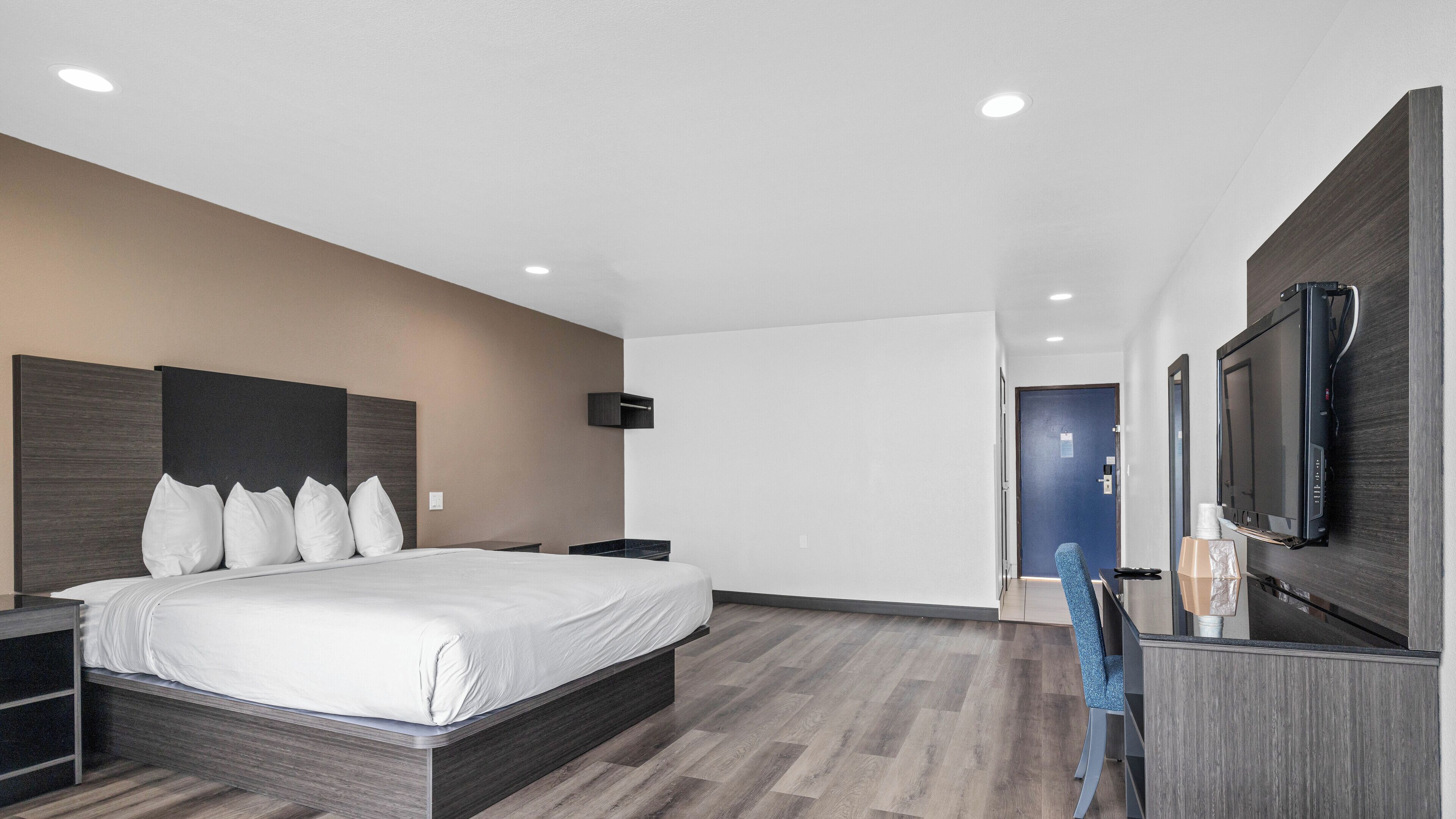 Una habitación de hotel moderna con una cama grande, un televisor de pantalla plana montado en la pared y suelo de madera.
