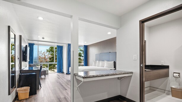 A modern hotel room with a bed, a desk, a TV, and a view of the outdoors. - Motel 6 Oceanside, CA Marina / Camp Pendleton (Oceanside)