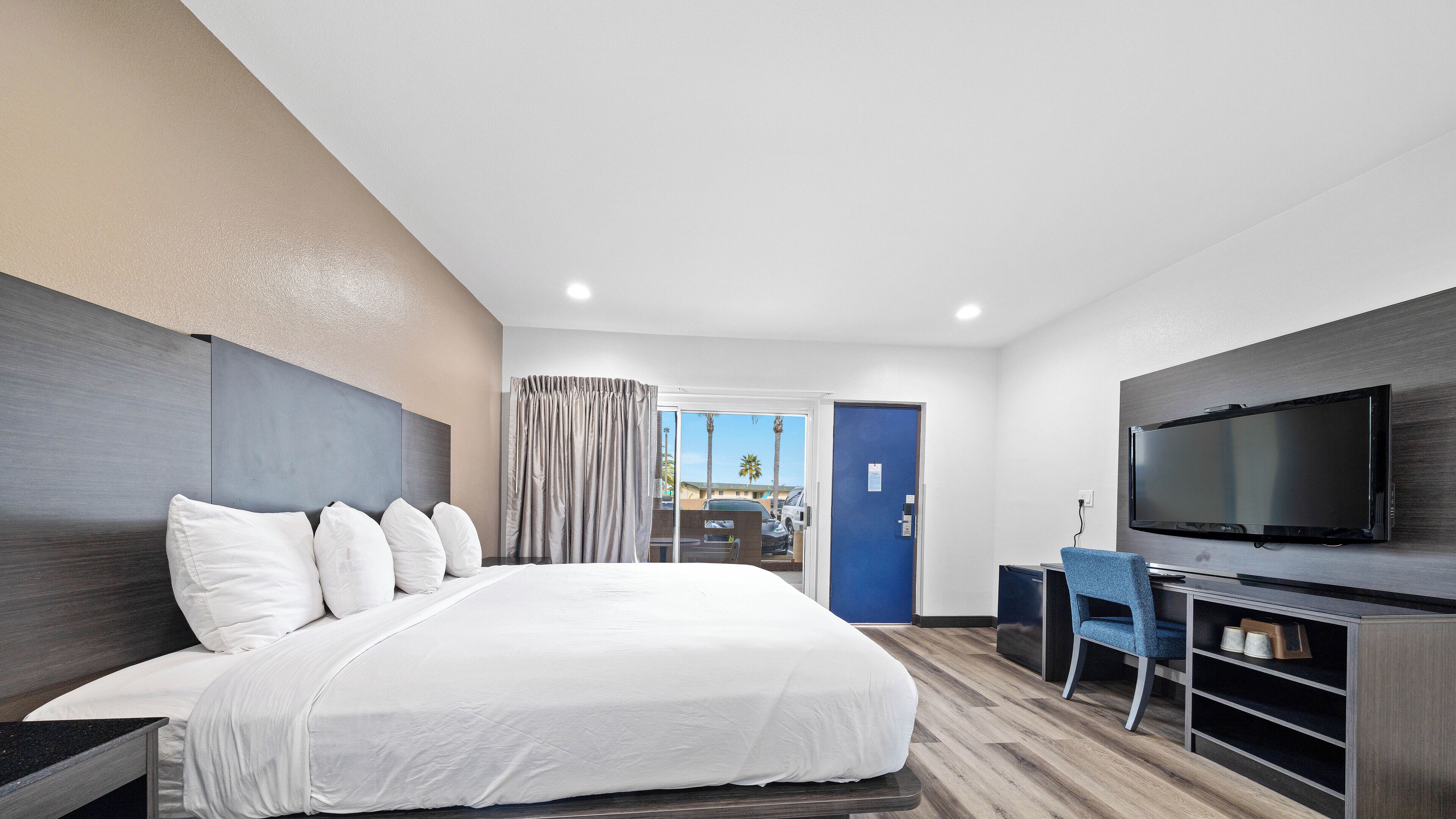 A modern hotel room with a large bed, a flat-screen TV, a desk, and a view of the outdoors.