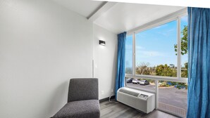A hotel room with a large window, a gray chair, and a wall-mounted air conditioner. - Motel 6 Oceanside, CA Marina / Camp Pendleton (Oceanside)