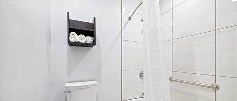 A modern bathroom with a toilet, a shelf with toiletries, and a shower with a curtain.