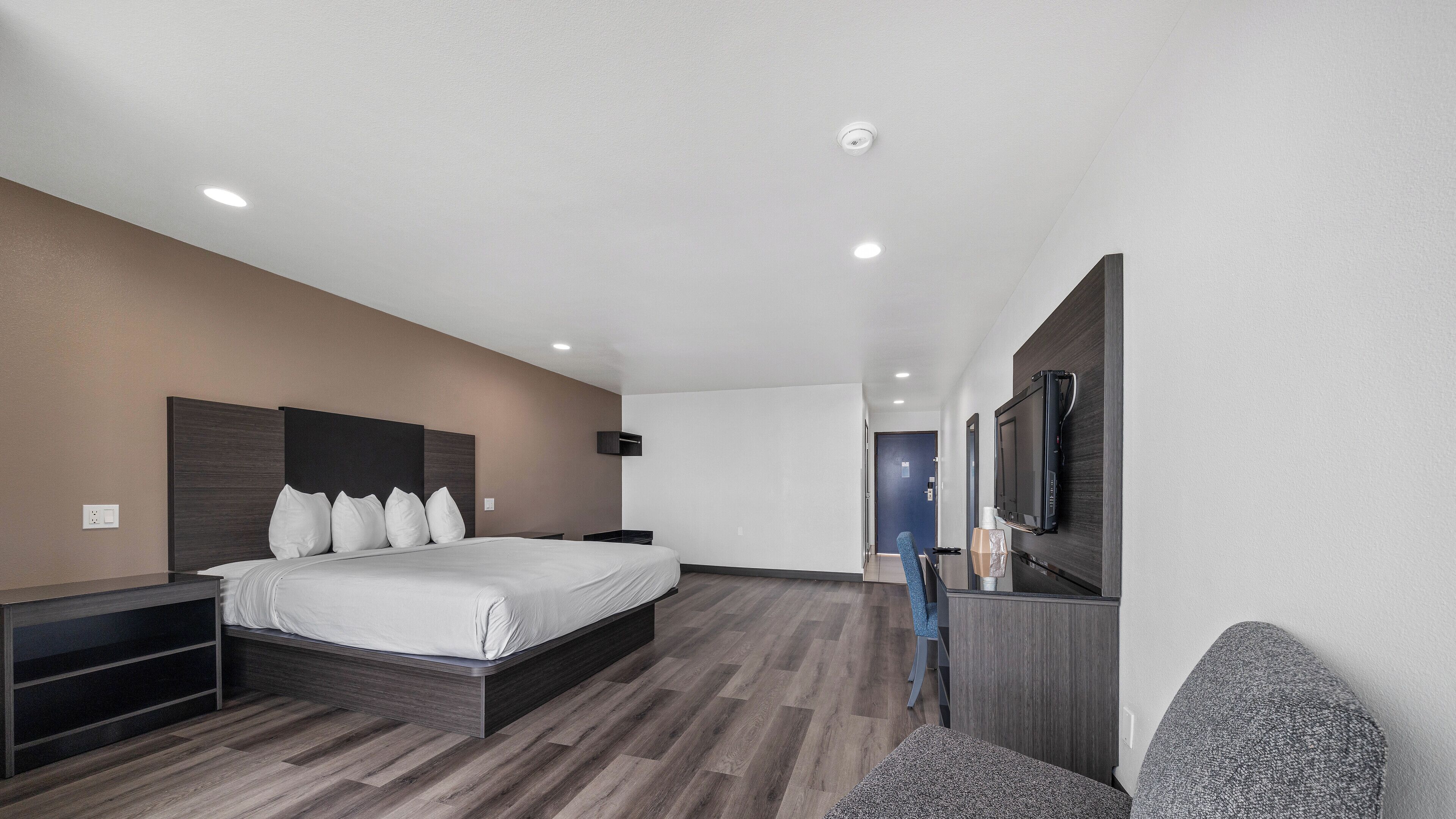 A modern hotel room with a large bed, a TV mounted on the wall, and a small seating area.