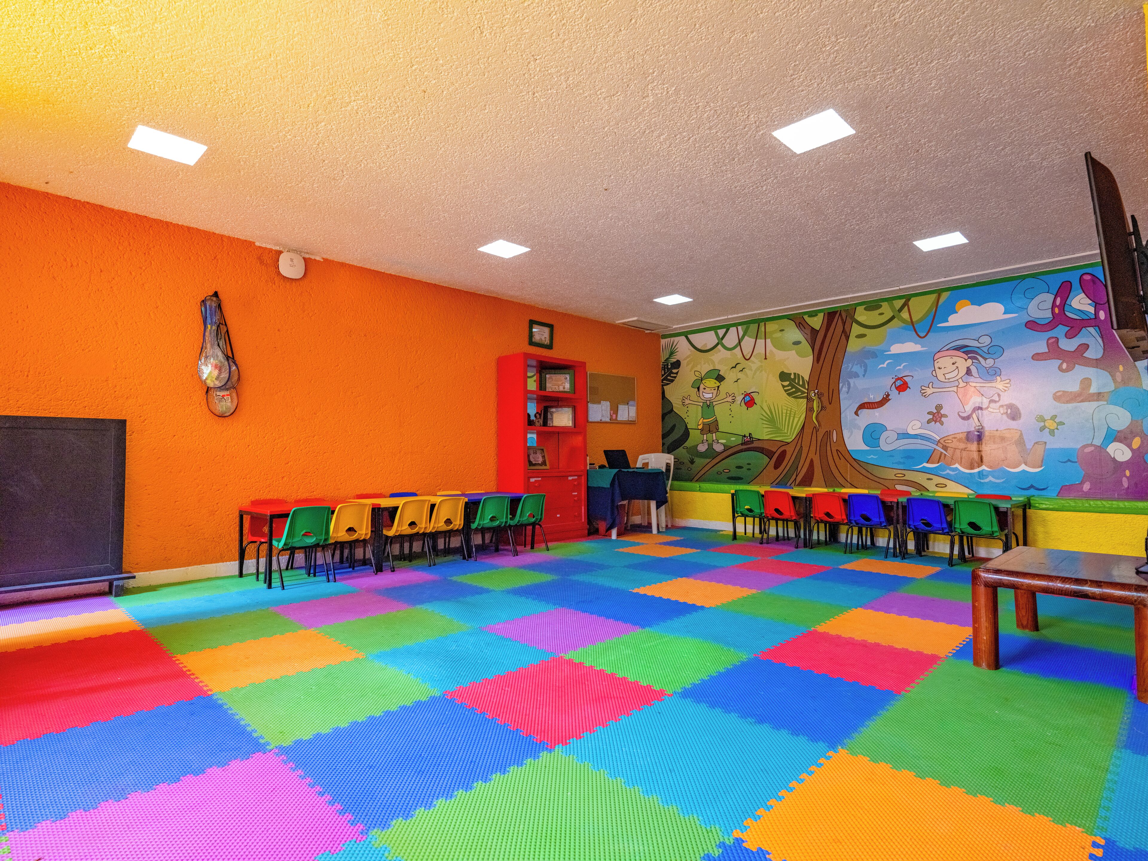 Una habitación luminosa y llena de color, con un piso llamativo, un mural y diversas opciones de asientos.