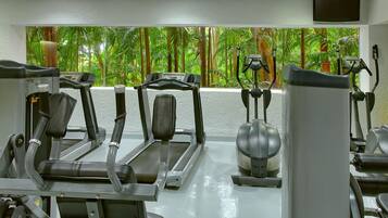Un gimnasio con cintas de correr, elípticas y una bicicleta estática, con un amplio ventanal que ofrece vistas tropicales.