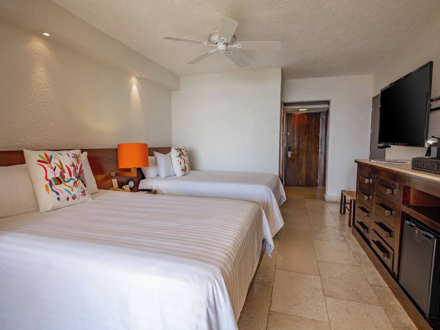 A hotel room with two beds, a ceiling fan, a TV, and a minibar.