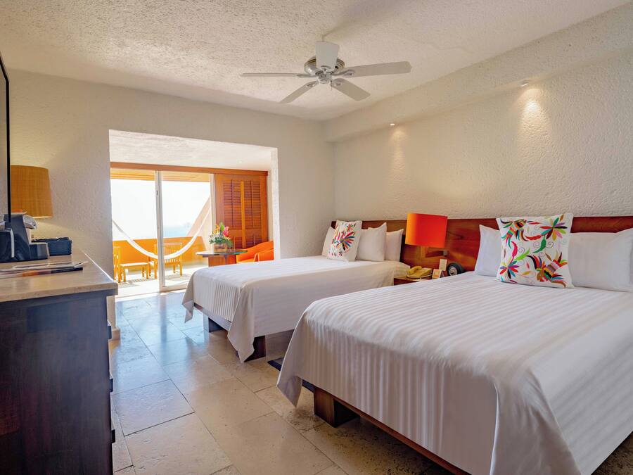 A hotel room with two beds, a desk with a lamp, a phone, and a window with a view of the outside.